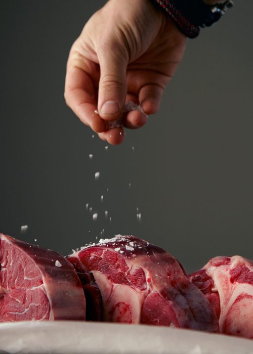 Hand is satling three fresh meat steaks with bone